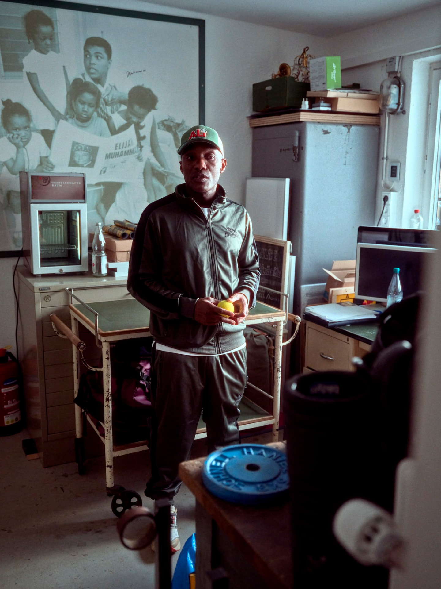 Coach Walu in the gym office, a Muhammad Ali photograph on the wall behind him